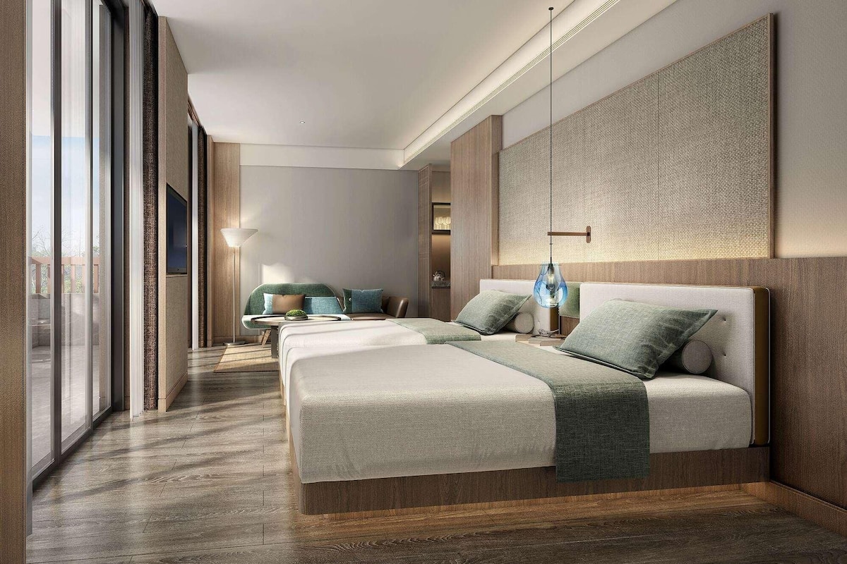 A modern hotel room with a large bed, a seating area, and a view through large windows.
