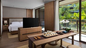 A modern hotel room with a bed, a TV, a dining table with a tray of food, and a large window with a view of greenery. - Wingate by Wyndham Hainan Chengmai (Chengmai)