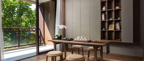 A modern interior with a wooden dining table, three stools, a potted orchid, and a bookshelf.