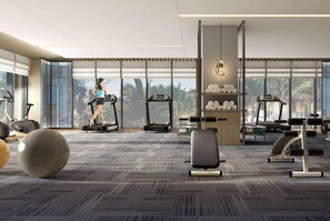 Un gimnasio moderno con cintas de correr, pelotas de ejercicio y un amplio ventanal con vistas a palmeras.