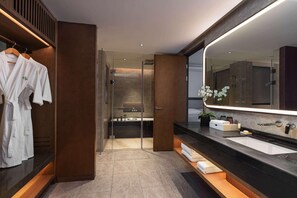 Un baño moderno con un espejo grande, muebles de madera oscura, cabina de ducha de vidrio y un banco de madera.