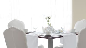 A dining table set for four with white chairs, a vase of flowers, and a white tablecloth. - Apollo Spa Resort (Golden Sands)