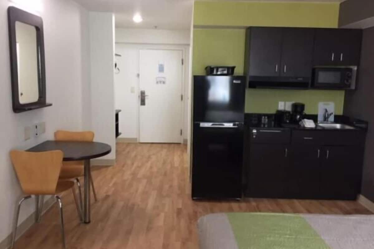 A compact hotel room with a kitchenette, a small dining area, and a bed.