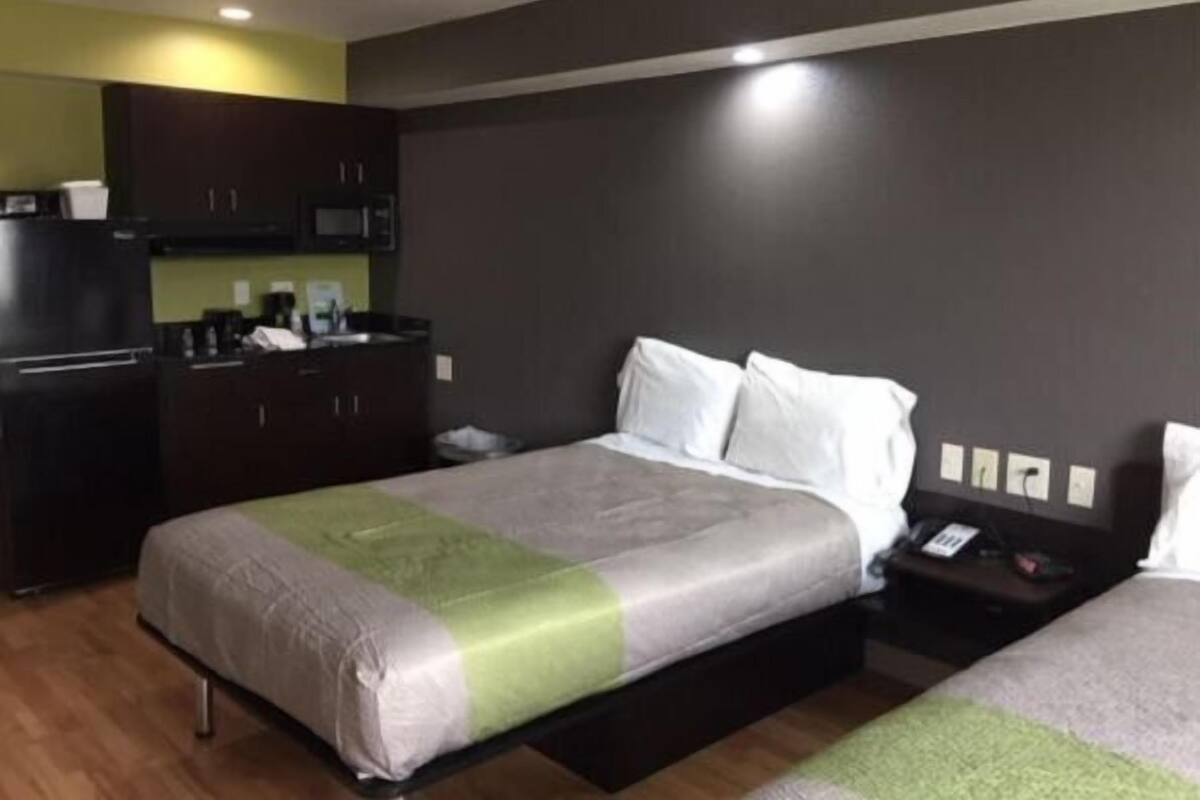 A hotel room with a bed, bedside table, and a kitchenette area.