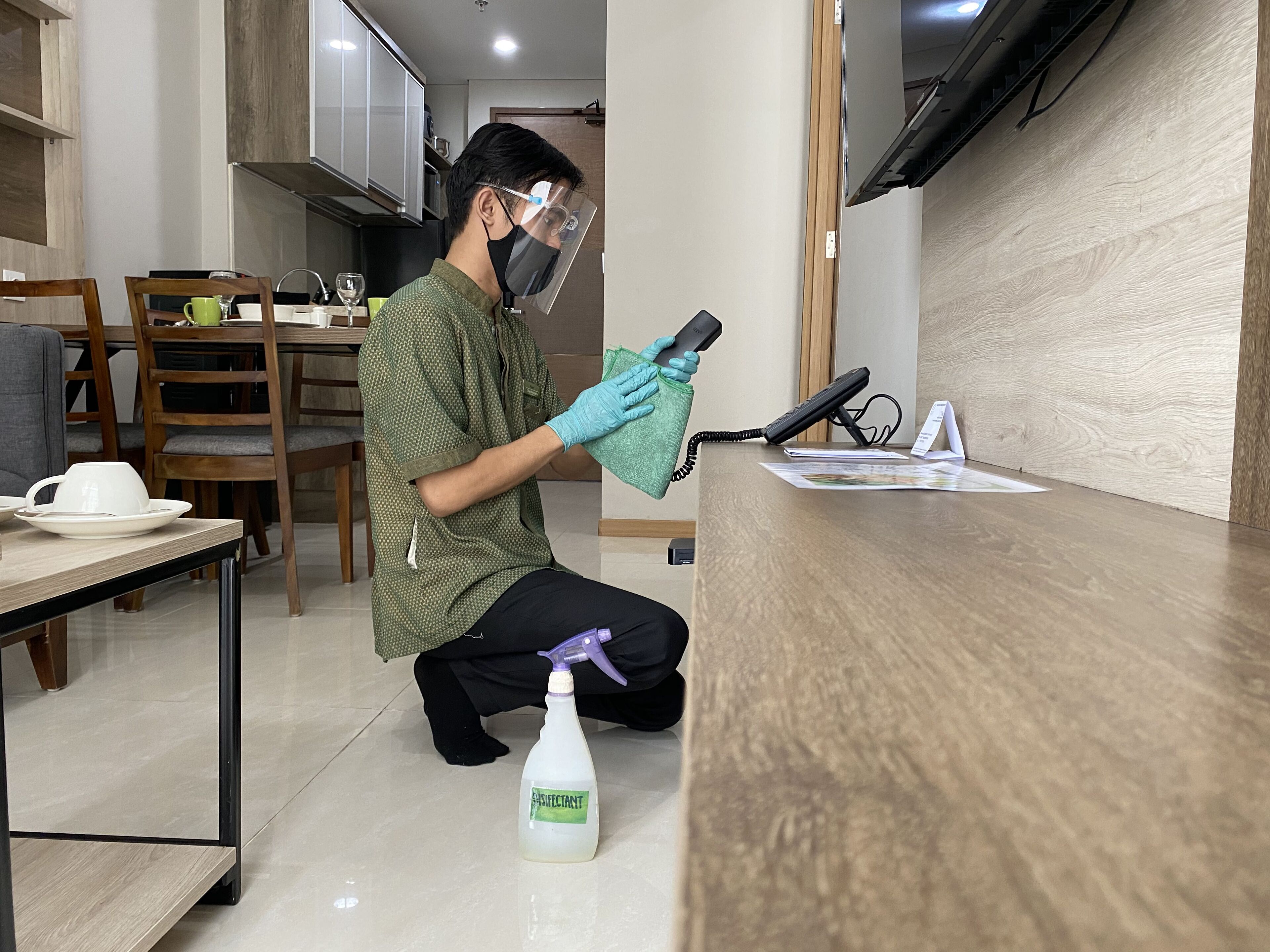 Una persona limpiando un mostrador de madera con una botella rociadora etiquetada como 'DESINFECTANTE'.
