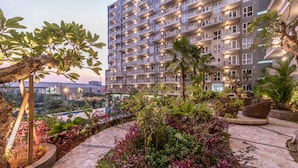 Un hôtel à plusieurs étages doté de balcons, d’un jardin aménagé avec différentes espèces de plantes et d’un sentier en pierre.