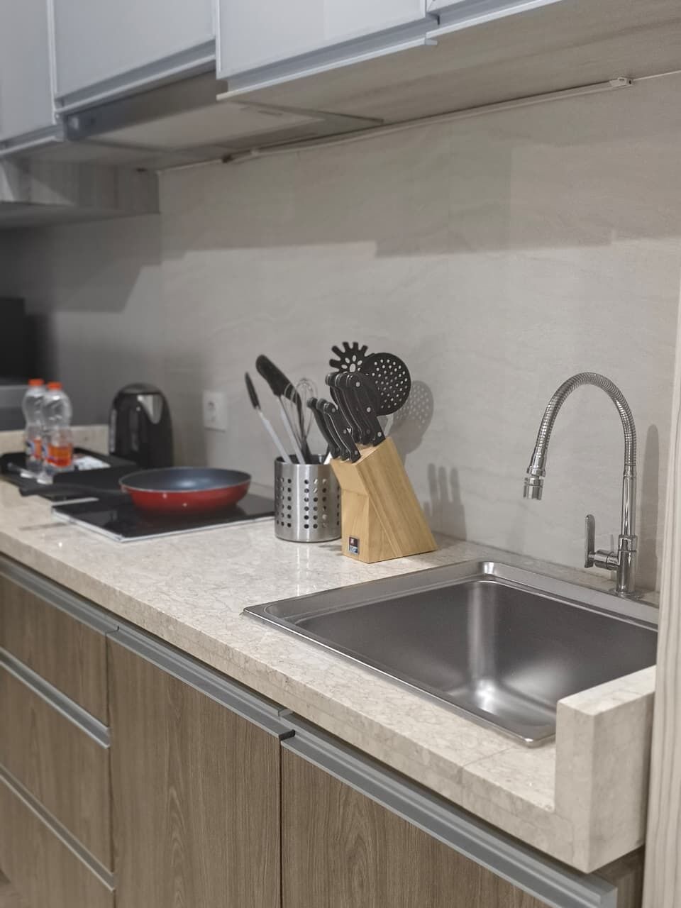 A kitchen with a stainless steel sink, a red frying pan, a coffee maker, and a knife block.
