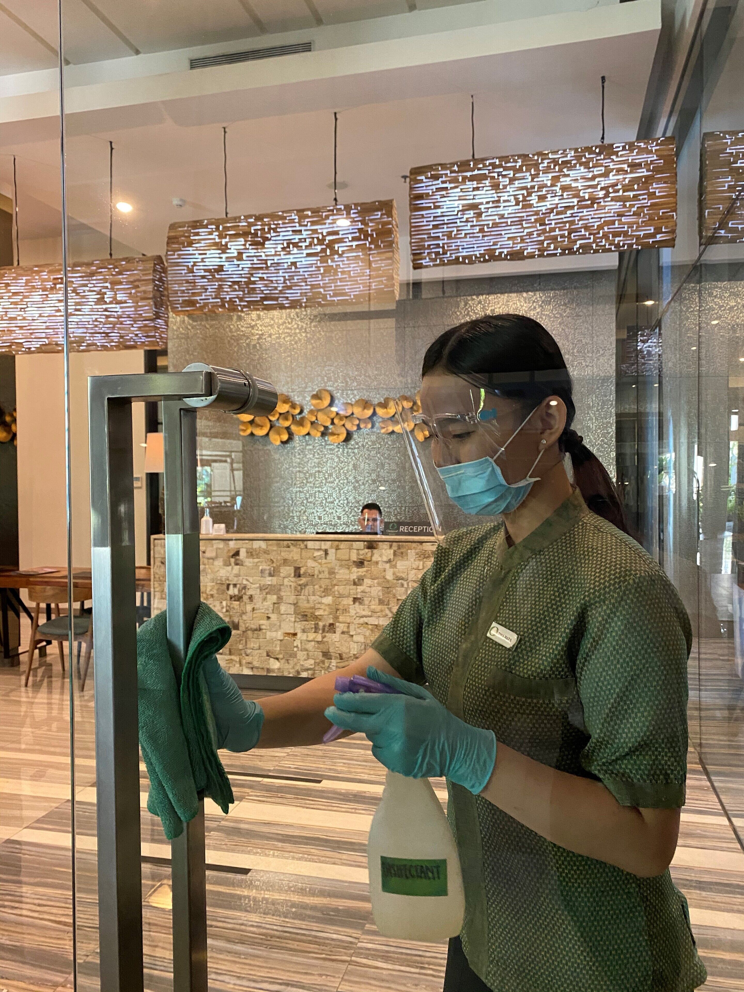 A person cleaning a glass partition with a cloth and a spray bottle.