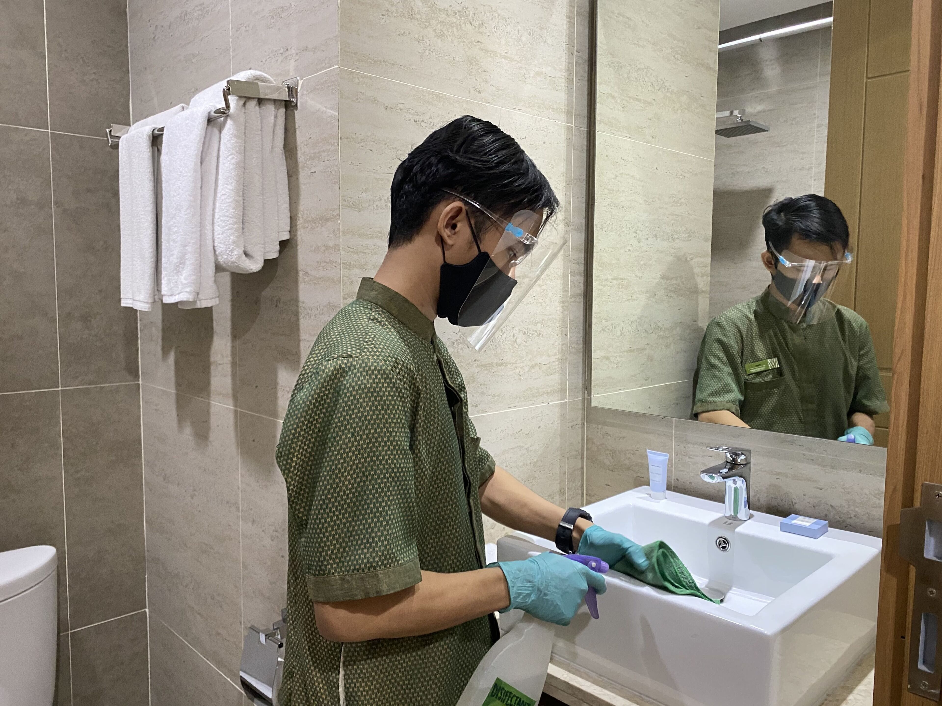 A person cleaning a sink in a bathroom with tiled walls and a mirror.