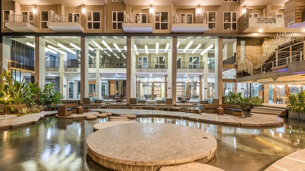 Un vaste atrium intérieur doté d’un élément aquatique central, de nombreux espaces de détente et d’une architecture moderne avec de grandes fenêtres et des balcons.