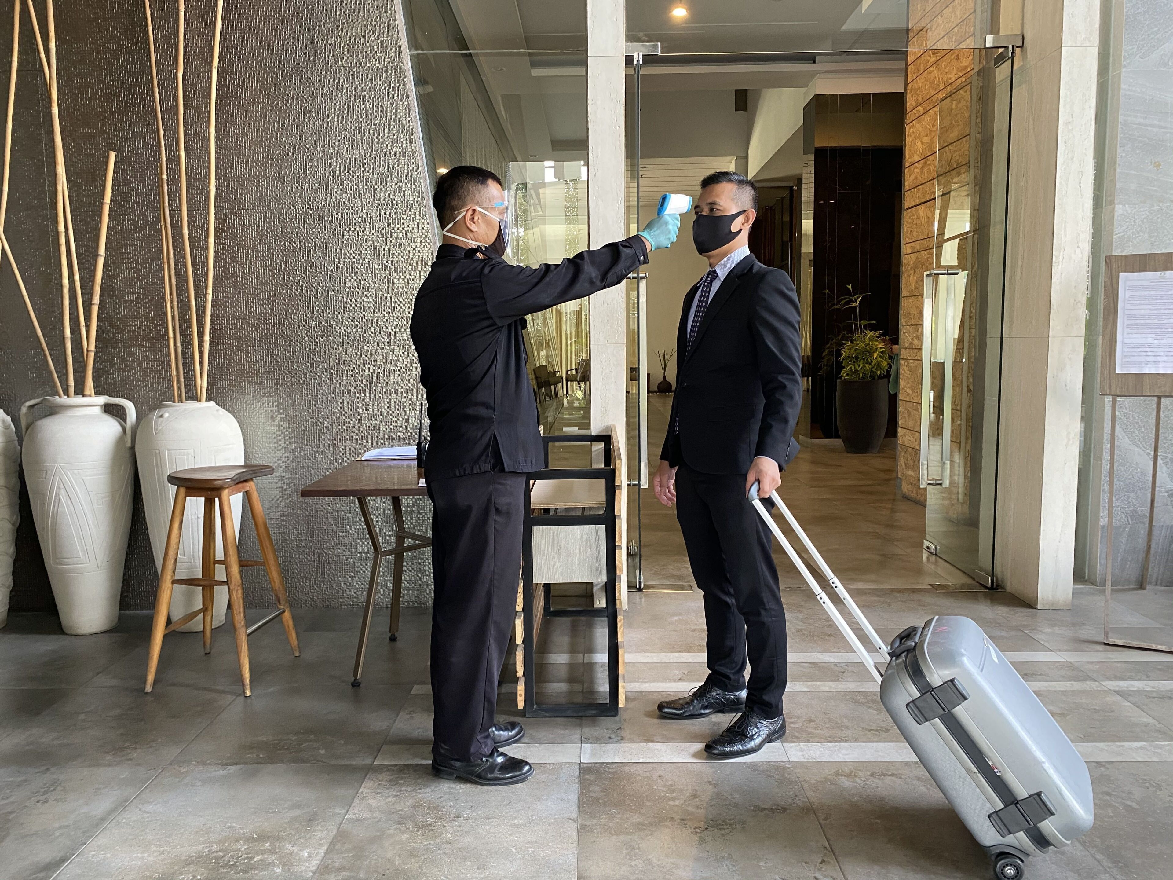 A man in a suit being screened with a handheld device in a hotel lobby with a modern interior, a table, and chairs.