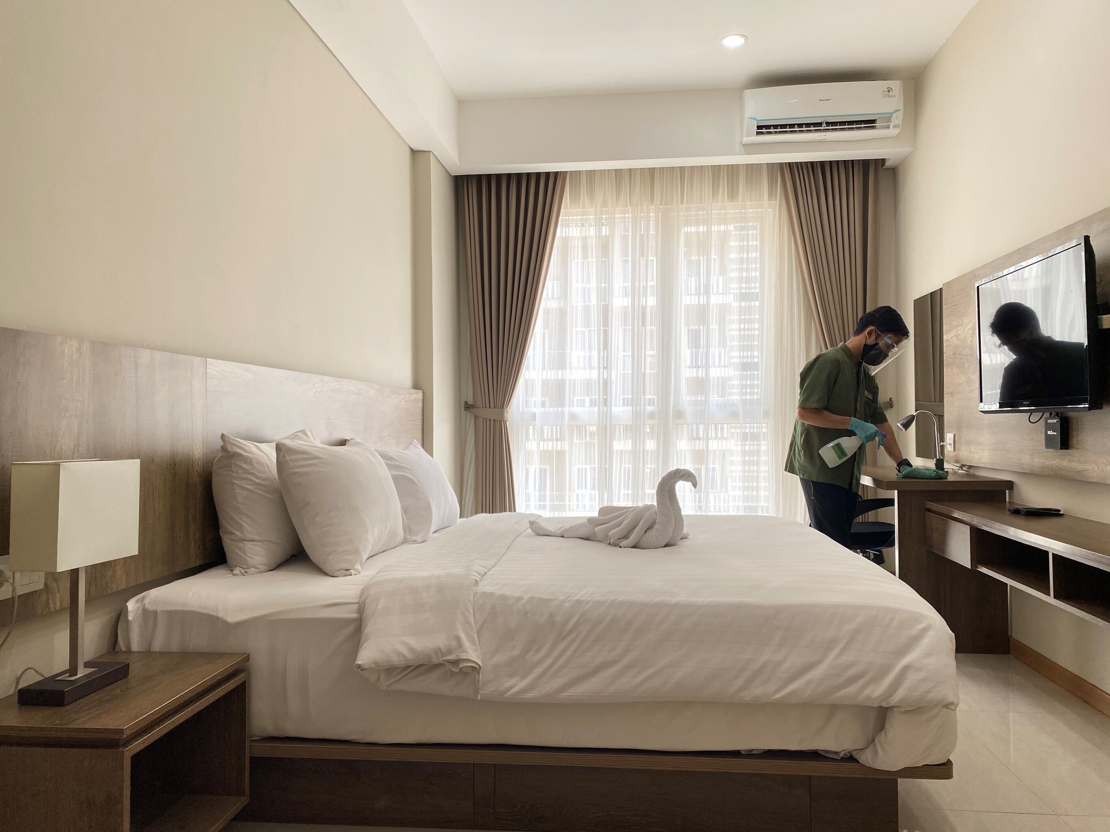 A hotel room with a neatly made bed, a television, a desk with a computer, and a large window with curtains.