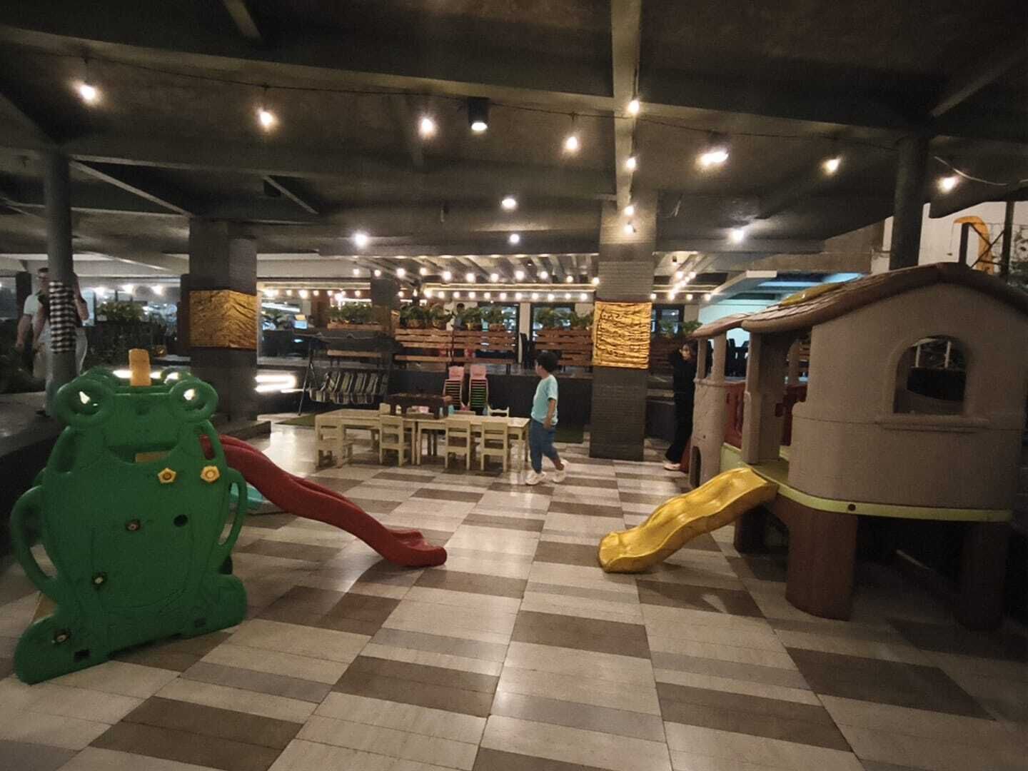 Un área de juegos interior con piso a cuadros, estructuras de juego y mesas.