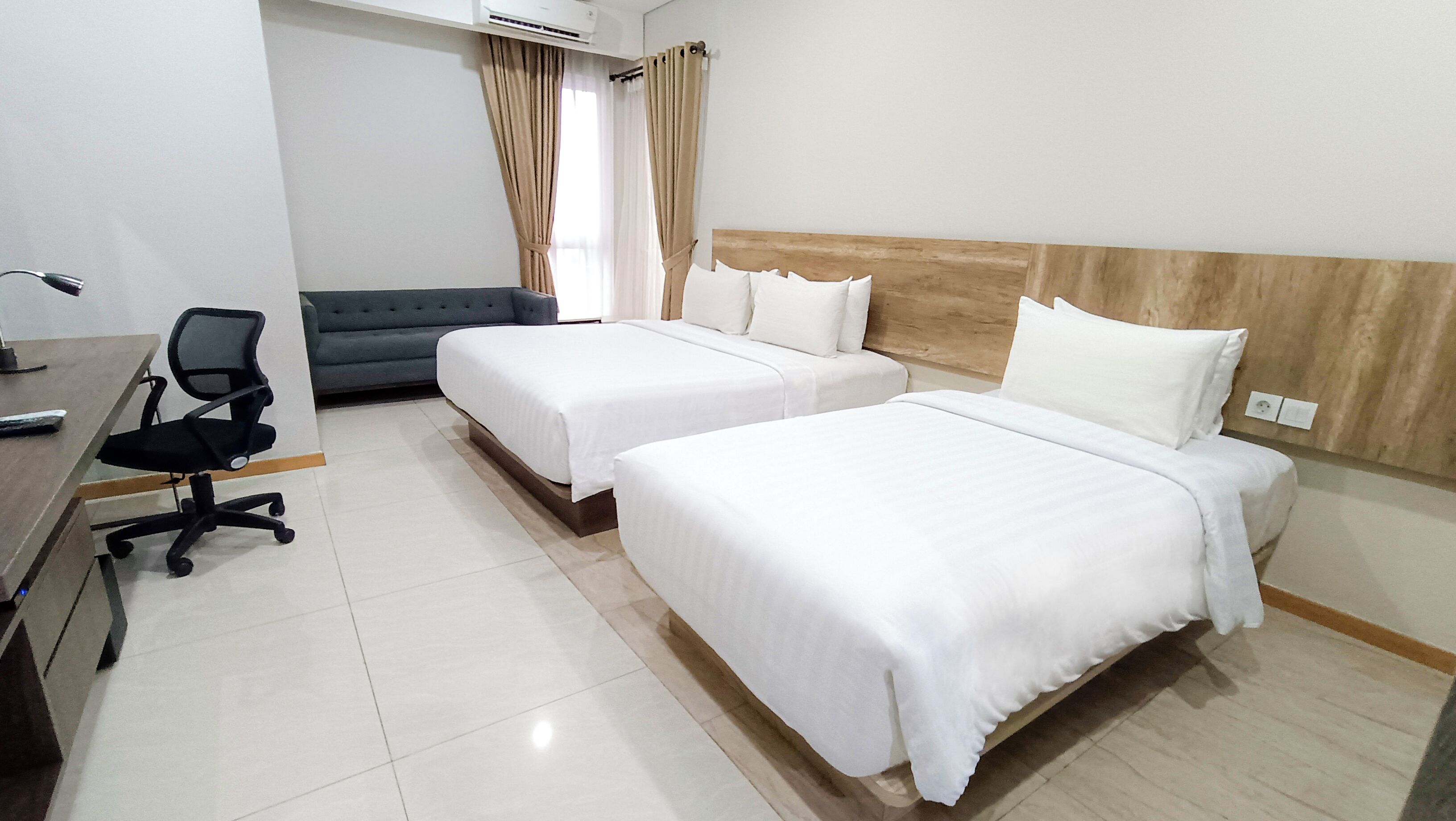 A hotel room with two beds, a desk, a chair, and a sofa.