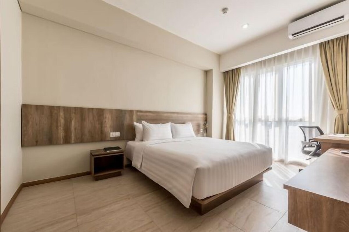 Une chambre d’hôtel avec un grand lit, une tête de lit en bois, une table de chevet, un bureau et une chaise.