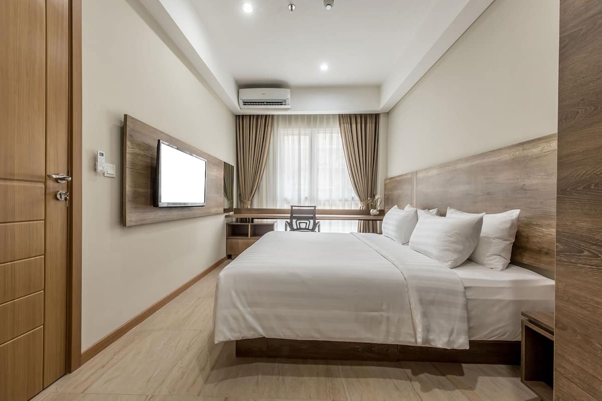 Ein modernes Hotelzimmer mit einem großen Bett, einem flachbildfernseher an der Wand, einem Schreibtisch mit Stuhl und einem Vorhangfenster.
