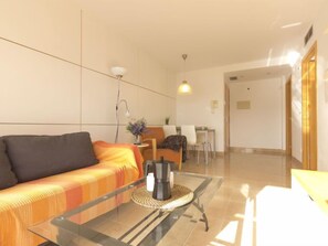 A modern living room with a glass coffee table, a sofa, and a dining area in the background.