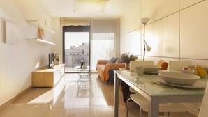 A modern apartment with a dining area, a sofa, a small kitchen, and a view of the city through the window. - Apartment Goleta by Interhome (Cambrils)
