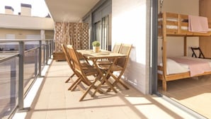 A balcony with a wooden table and chairs, a small potted plant, and a bunk bed with a pink blanket. - Apartment Goleta by Interhome (Cambrils)