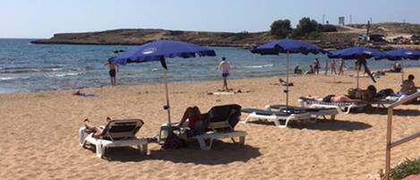 A beach with sun loungers and umbrellas, a sandy shore, and the sea in the background.