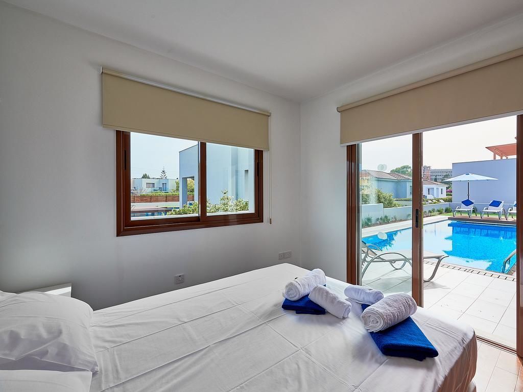 Une chambre d’hôtel avec un lit, une fenêtre donnant sur une piscine et un espace extérieur aménagé, ainsi qu’un balcon avec vue sur la piscine.