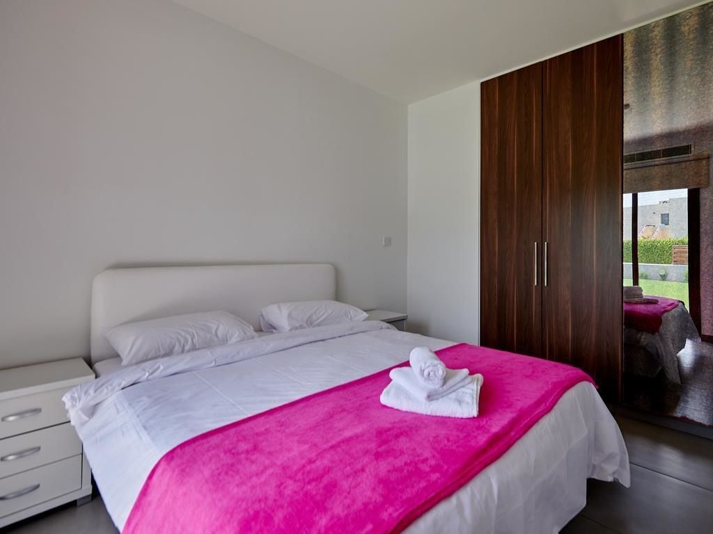 A modern bedroom with a large bed, white bedding, a pink throw blanket, and a wooden wardrobe.