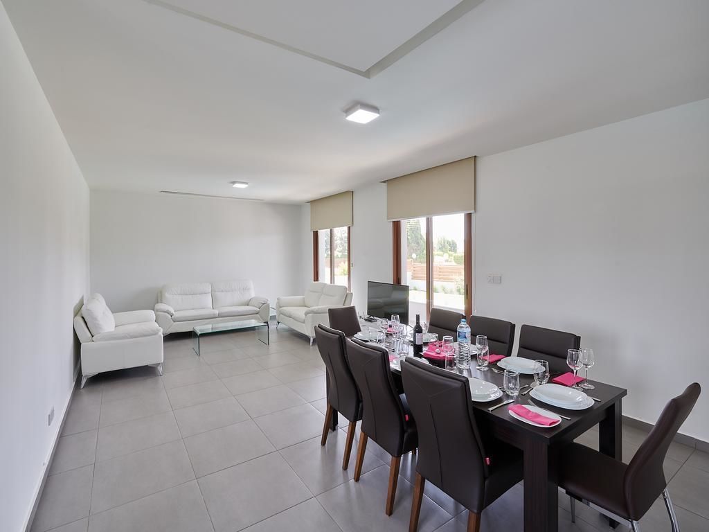 A modern dining area with a table set for four, white sofas in the background, and a TV on a stand.