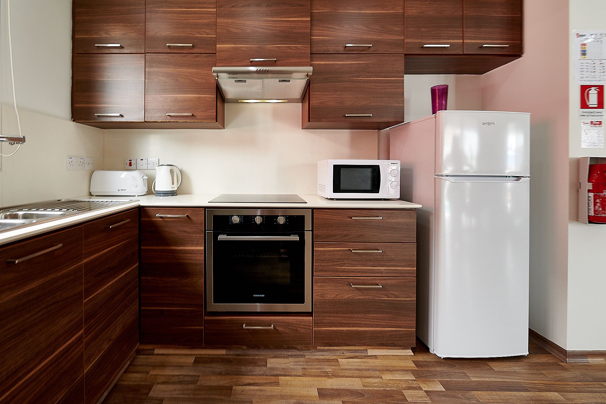 A compact kitchen with wooden cabinets, a built-in oven, a microwave, and a refrigerator.