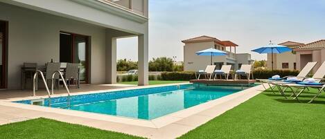 Ein moderner Außenpoolbereich mit klarem, blauem Wasser, Liegestühlen und Sonnenschirmen.