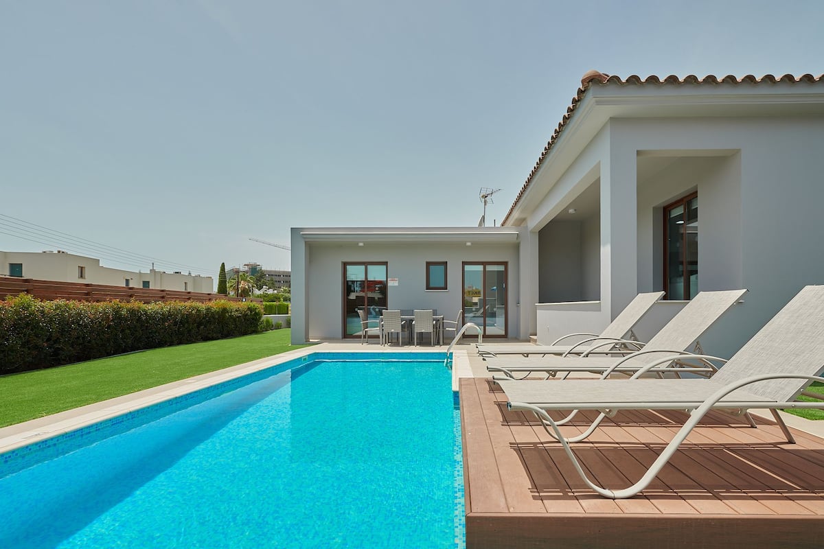 Ein Swimmingpool mit Liegestühlen, eine kleine Terrasse und ein Gebäude mit großen Fenstern.
