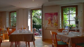 Un espace repas avec des tables disposées pour accueillir quatre personnes, des chaises en bois et une grande affiche accrochée au mur.