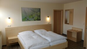Un lit bien fait, avec du linge de lit blanc, une tête de lit en bois et un tableau aux motifs verts abstraits accroché au mur.