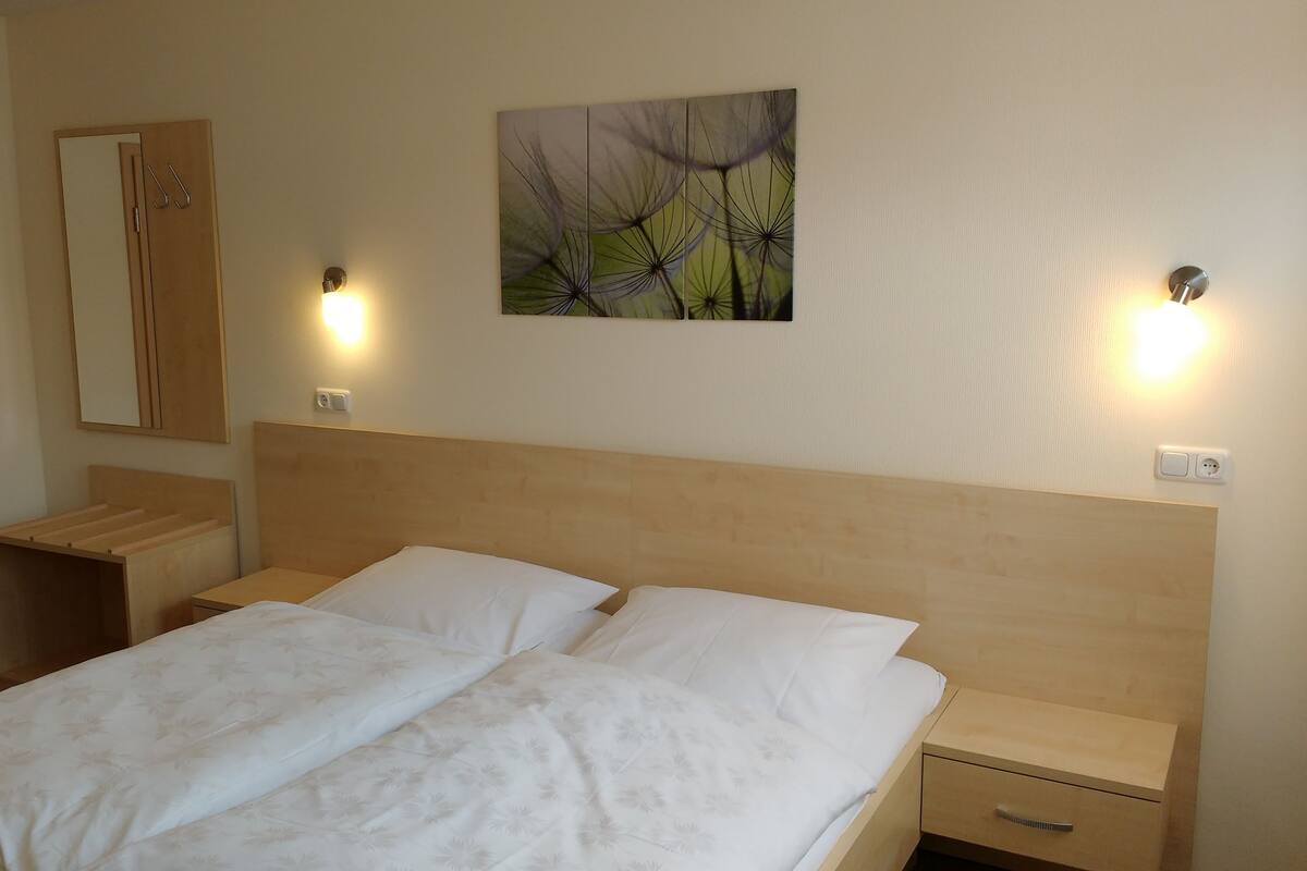 Ein Hotelzimmer mit einem Doppelbett, einem Holz-Kopfteil, Nachttischen, einem Schminktisch und einer an der Wand befestigten Lampe.