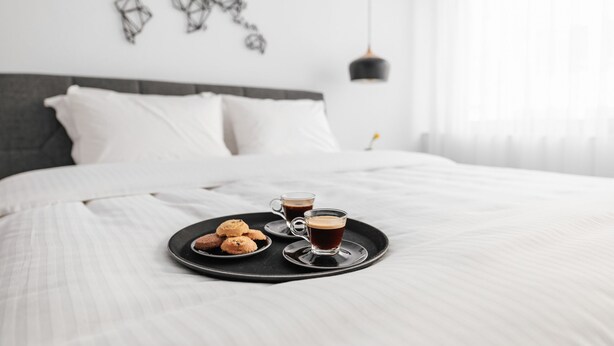 A neatly made bed with a tray of cookies and a cup of coffee on a black tray. - Evapollo (Thessaloniki)