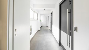 A modern hallway with a grey tiled floor, white walls, and a door with a black handle. - Evapollo (Thessaloniki)