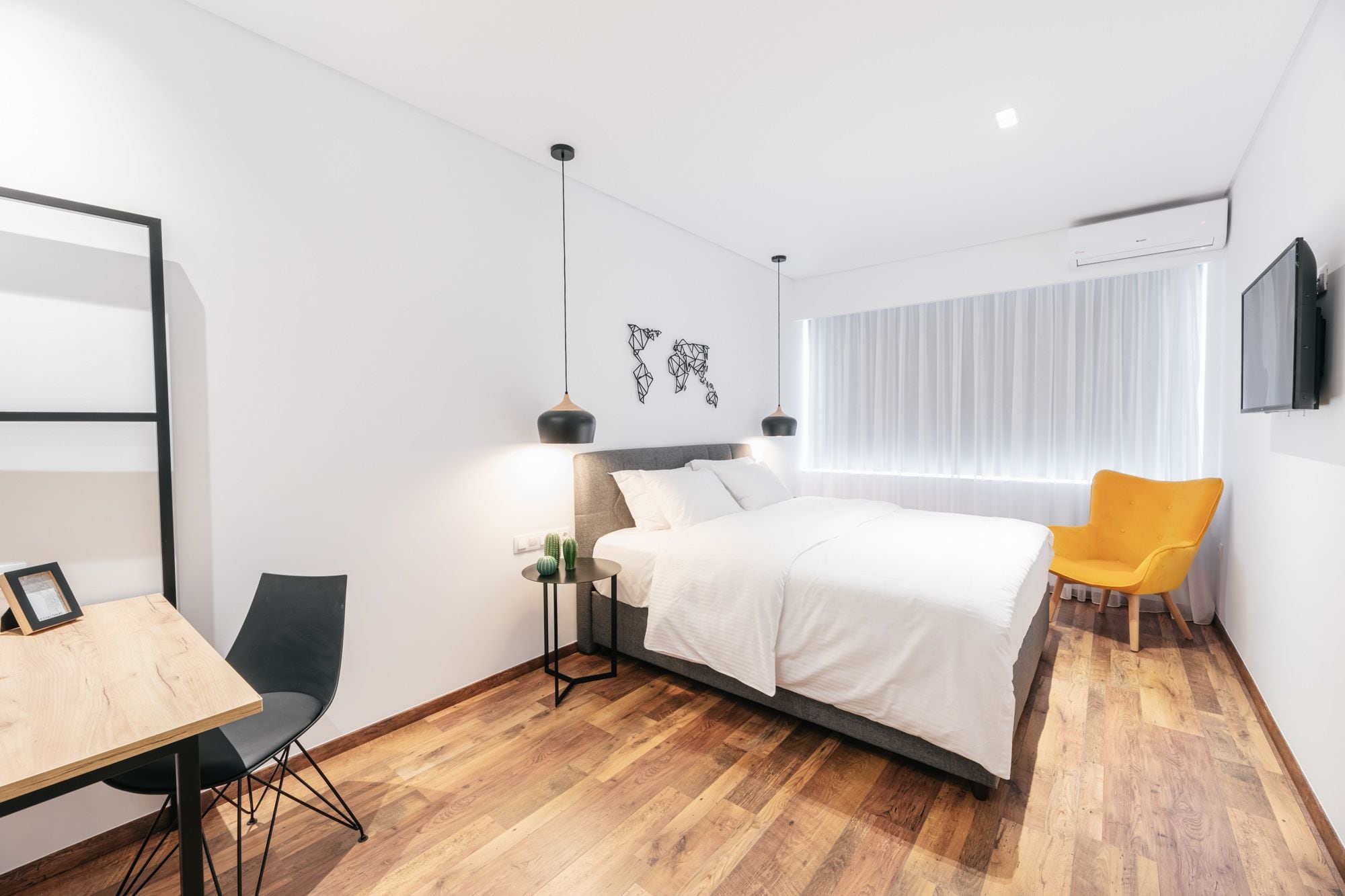 A modern hotel room with a bed, a desk, a chair, and a TV.