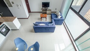 A modern living room with a blue sofa, a coffee table, and a TV. There are blue chairs and a kitchen area in the background. - PrimeTime Depto en Las Mercedes (Asunción)