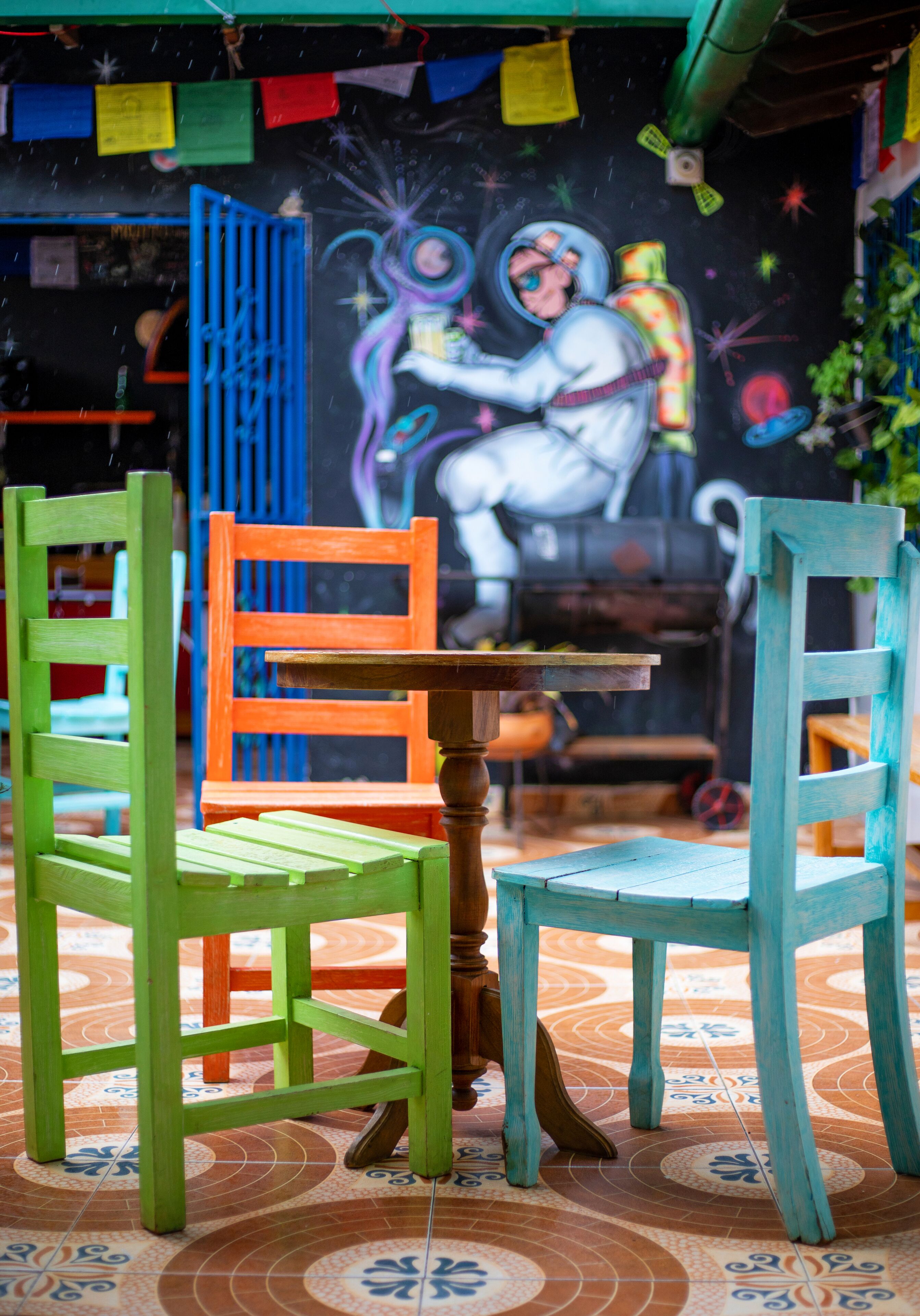 A dining area with two chairs and a table, a mural with an astronaut, and colorful tiles on the floor.