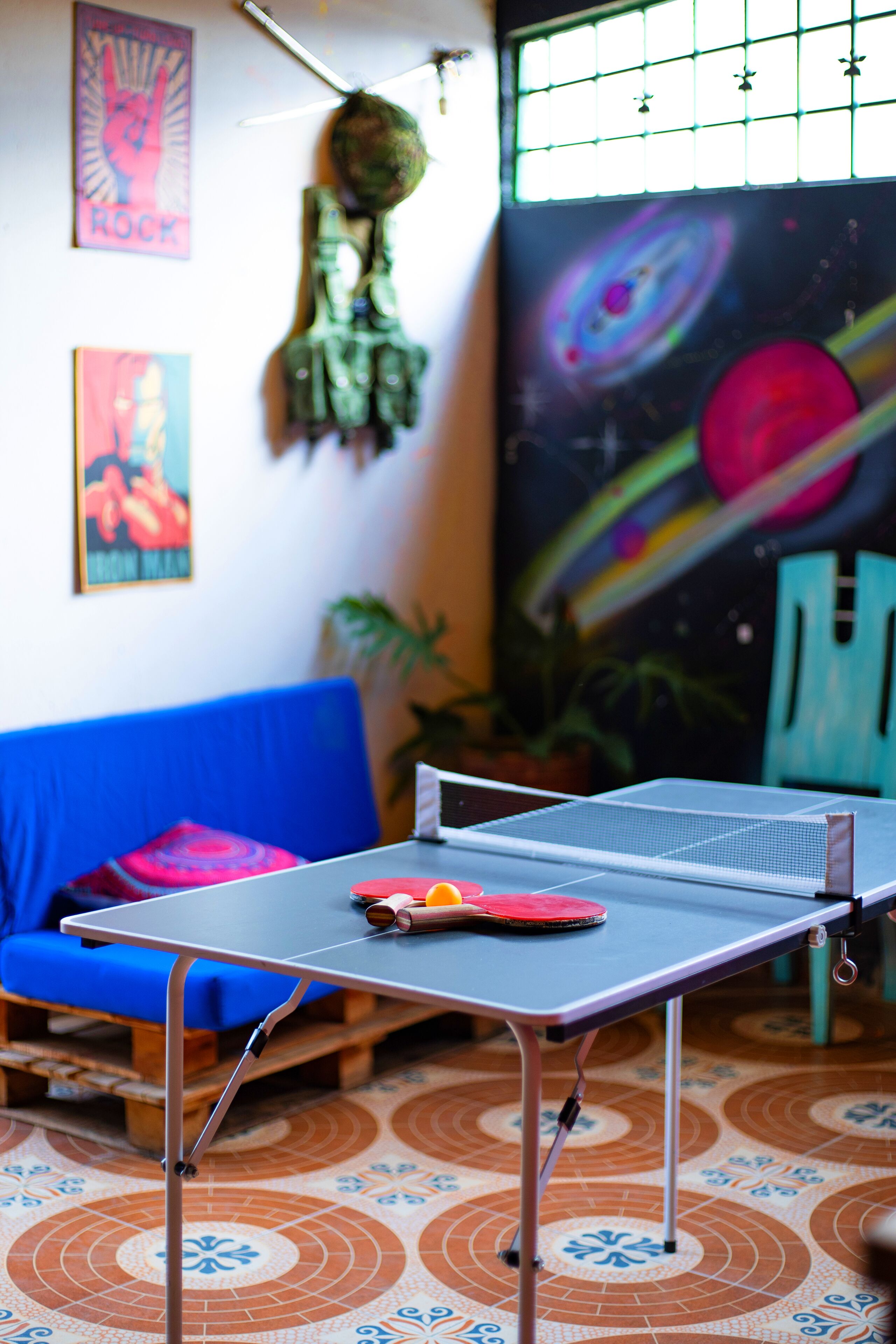 Une table de ping-pong dans une pièce avec un canapé bleu, une fresque murale sur le thème de l’espace et une décoration suspendue.