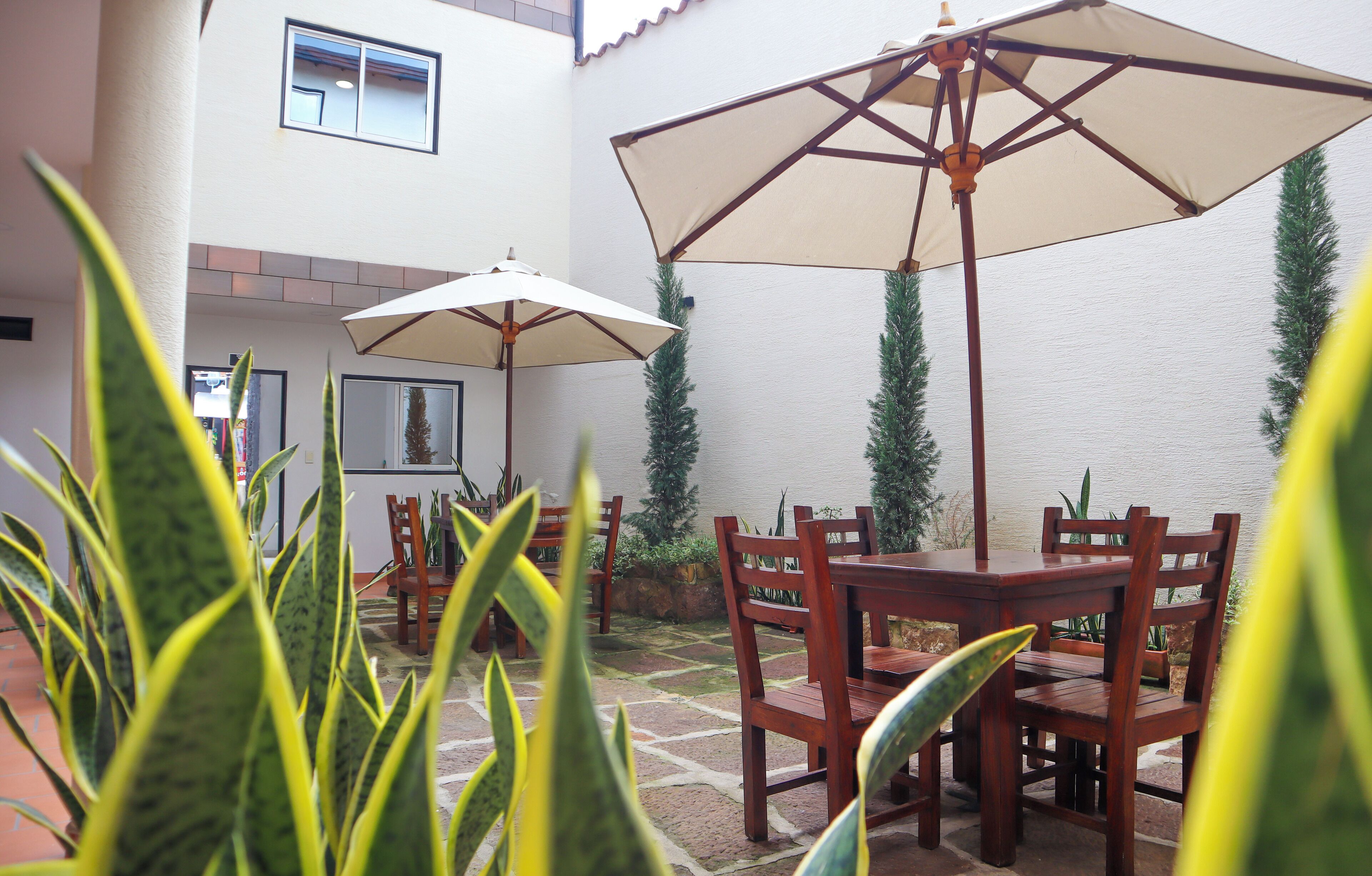 A patio area with wooden tables and chairs, two large umbrellas, and potted plants.