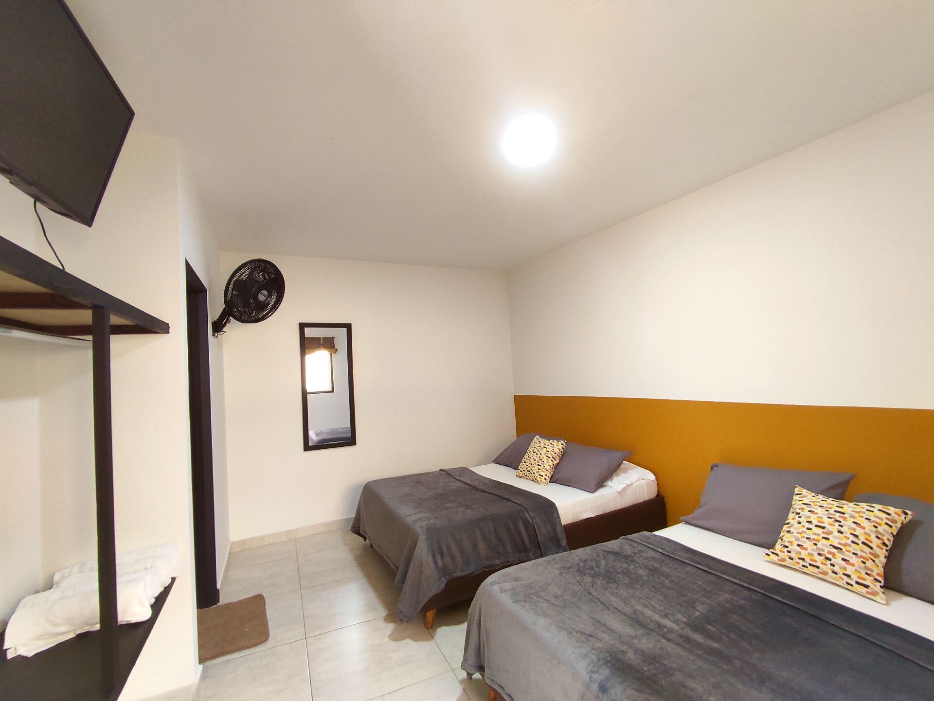 Una habitación con dos camas, un espejo, un ventilador de techo y un televisor.