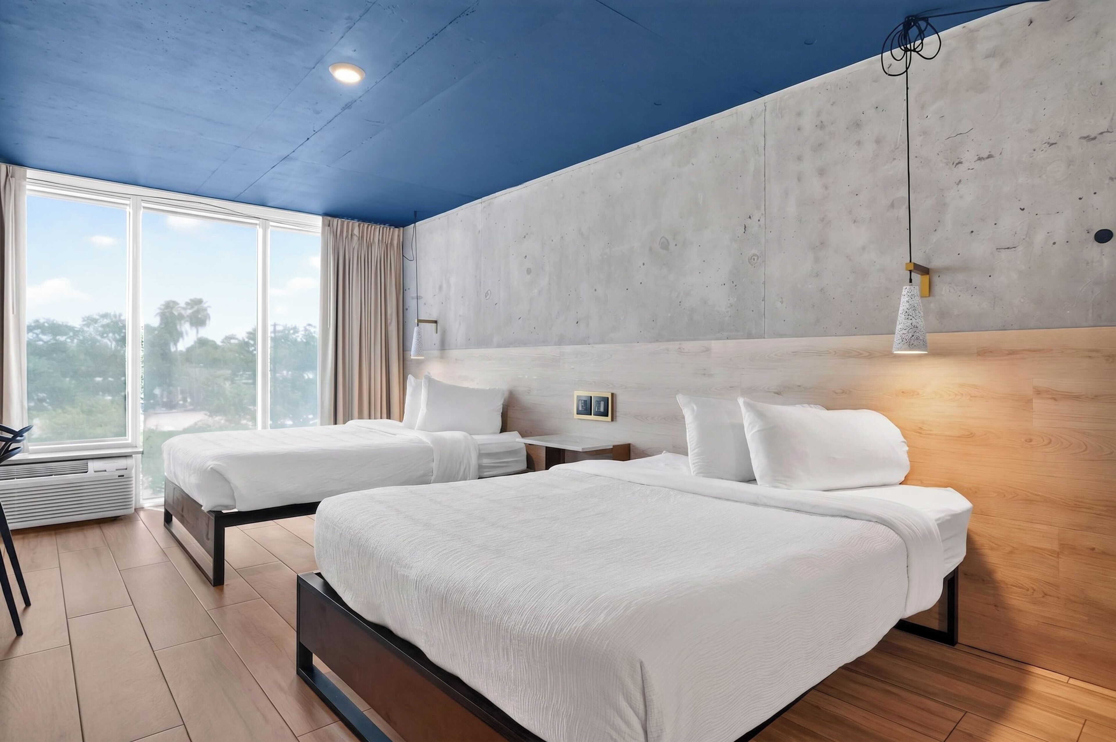 A modern bedroom with two beds, a large window, and a view of the outdoors.