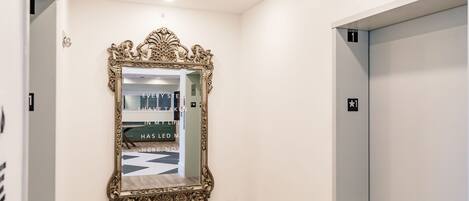 A hallway with a large ornate mirror, a wooden floor, and an elevator marked with an "Elevator 1" sign.