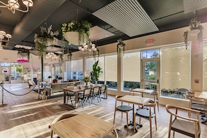 A spacious indoor area with wooden tables and chairs, large windows, and hanging plants. - Kompose Boutique Hotel (Sarasota)