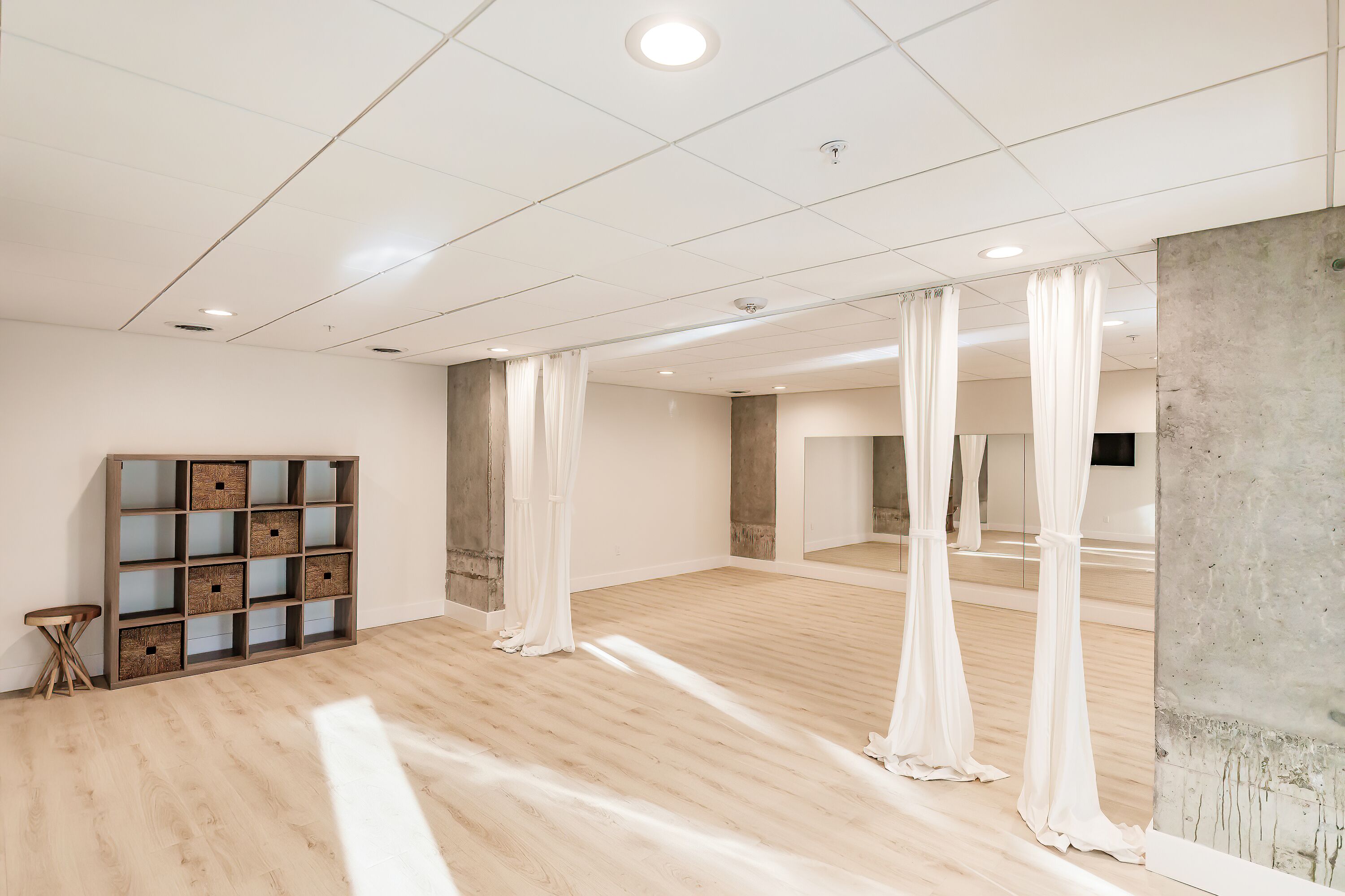 A spacious room with a wooden floor, a large mirror, and a wooden storage unit.