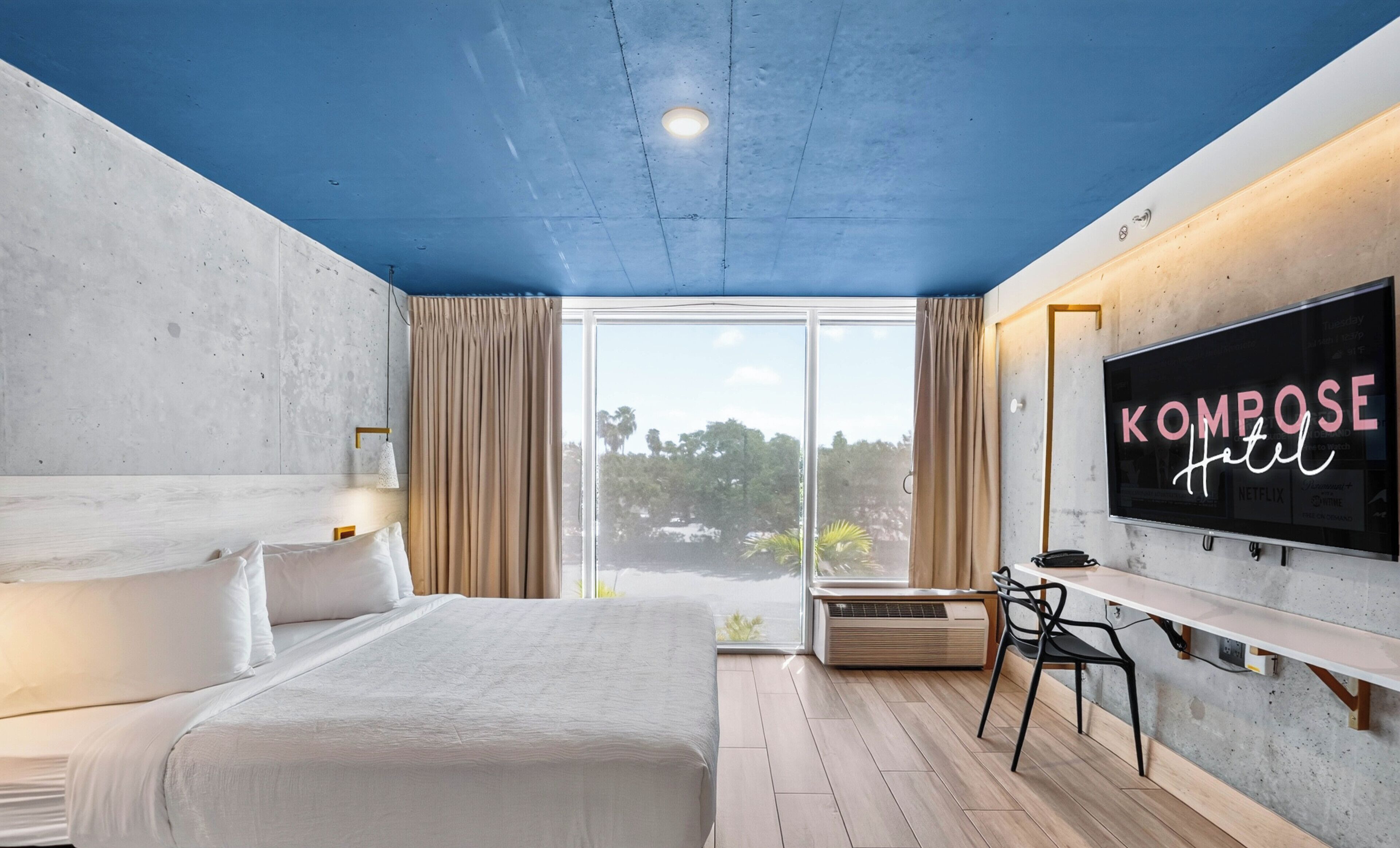 Habitación de hotel con cama, televisión montada en la pared, ventana con cortinas y vista a zonas verdes.