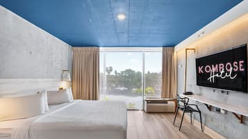 Habitación de hotel con cama, televisión montada en la pared, ventana con cortinas y vista a zonas verdes.