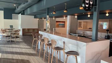 A modern bar area with a marble counter, wooden chairs, pendant lighting, and a sign indicating AM and PM service hours.