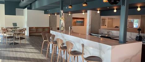 A modern bar area with a marble counter, wooden chairs, pendant lighting, and a sign indicating AM and PM service hours.