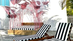 Two lounge chairs with striped cushions, a wooden bench, and a decorative metal plant structure.